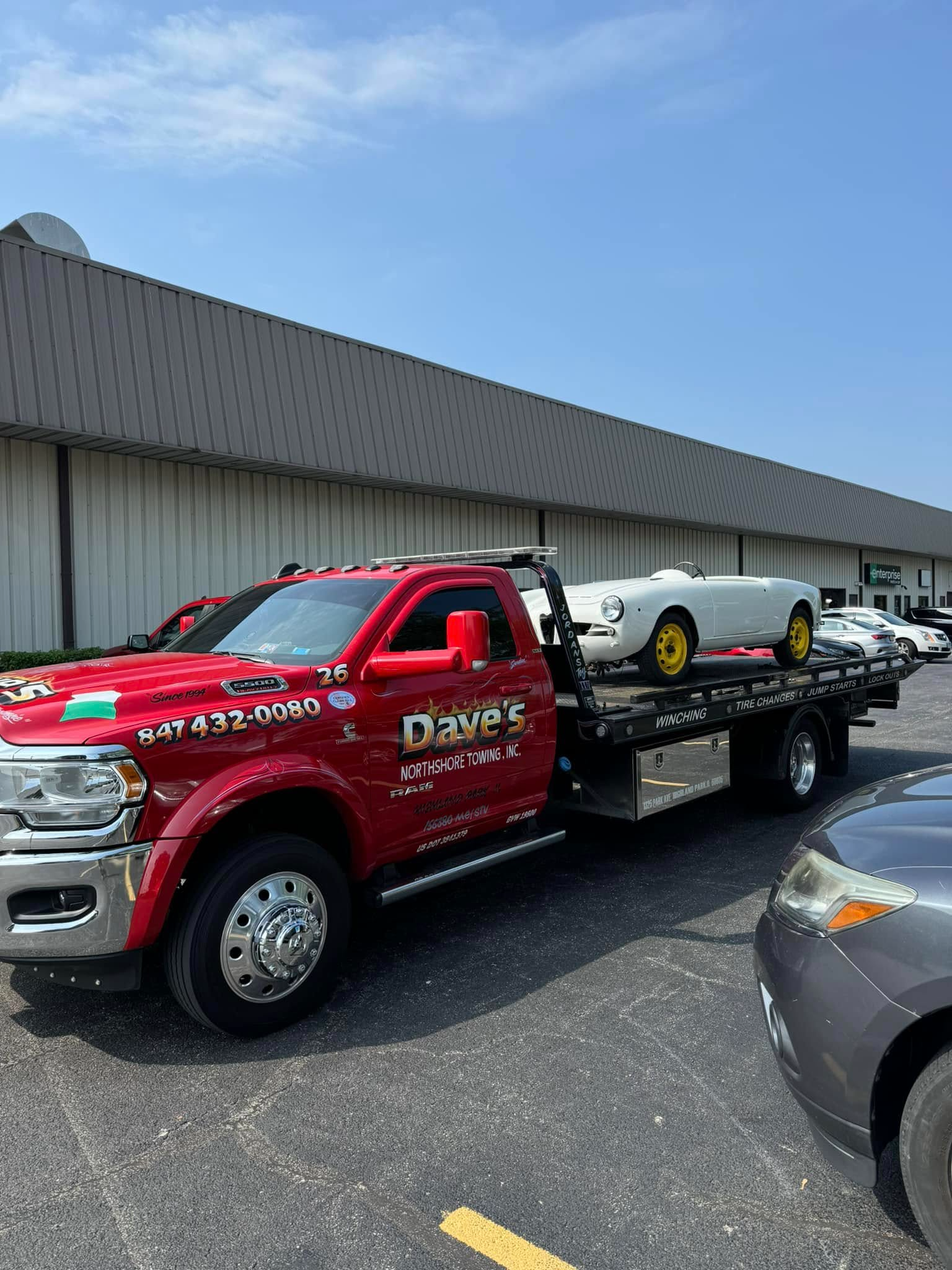 A red tow truck is carrying a white sports car.