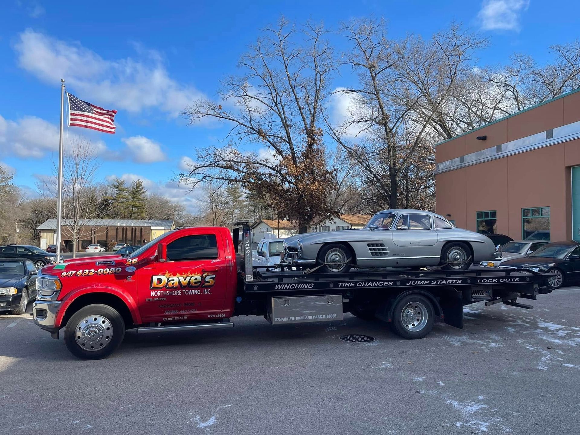 A tow truck is carrying a silver car on the back of it.