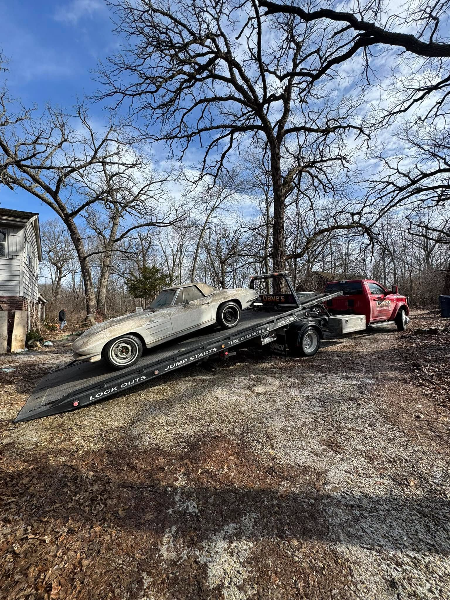 A white car is being towed by a red tow truck.