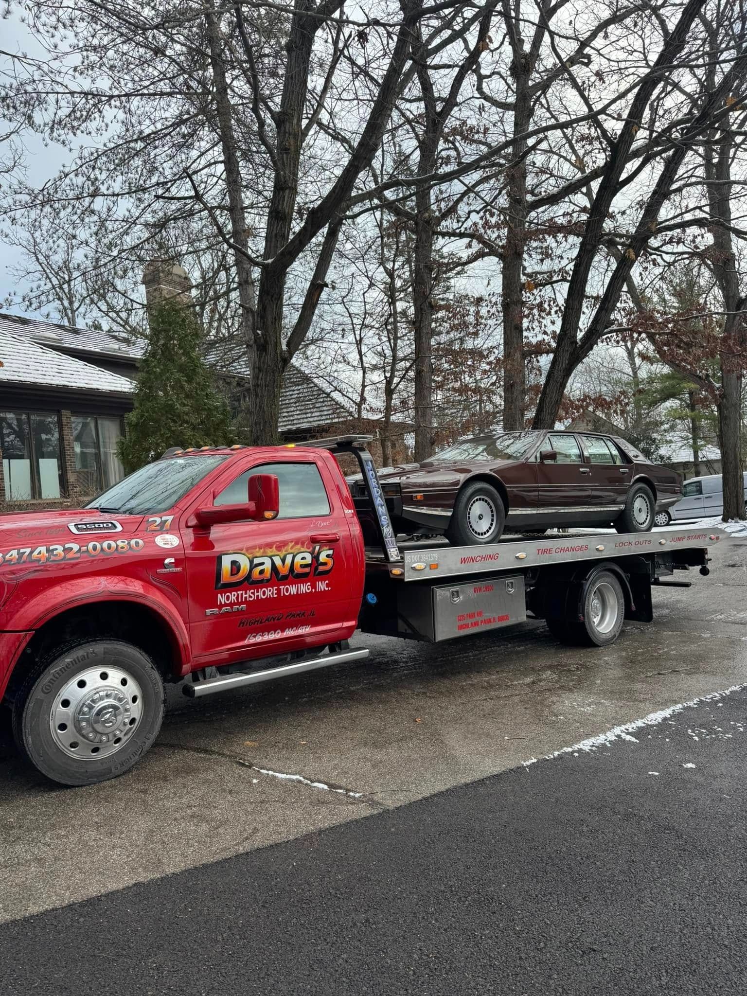 A red tow truck is towing a car on the back of it.