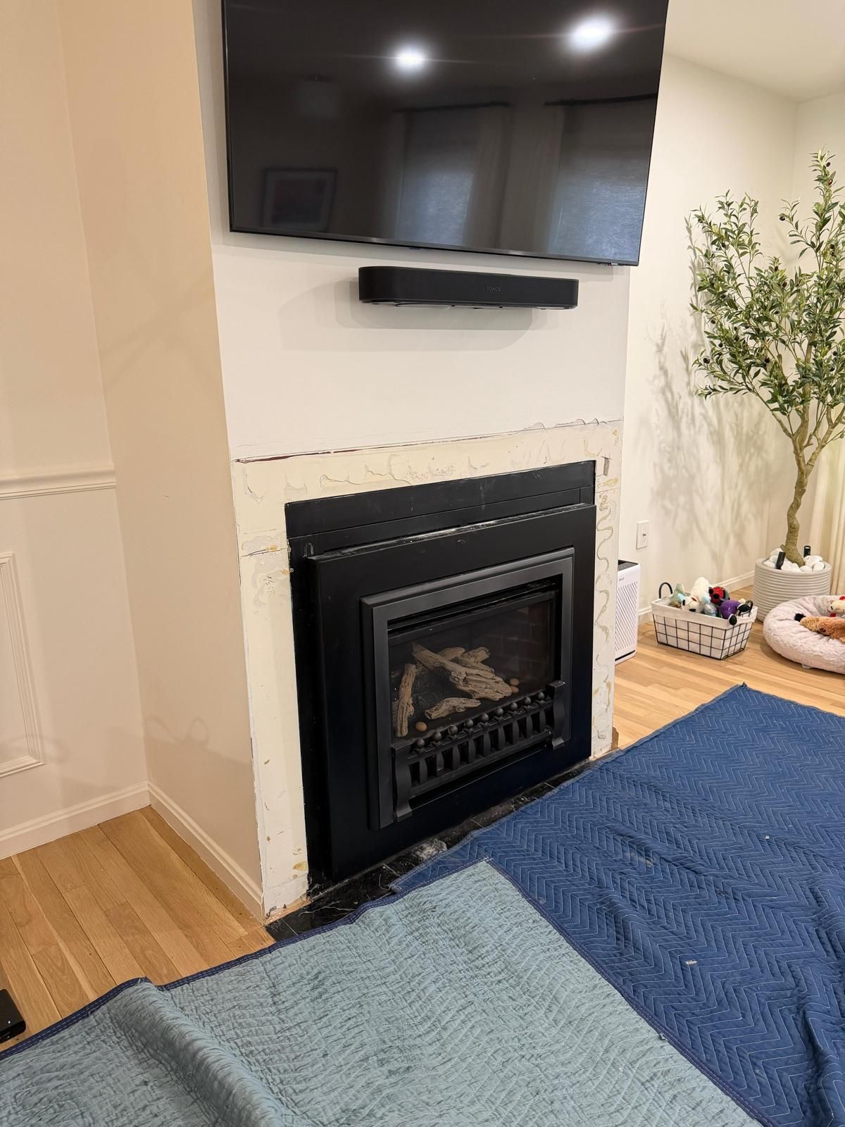 Fireplace with black surround, mounted TV, soundbar, and blue blankets in a room.