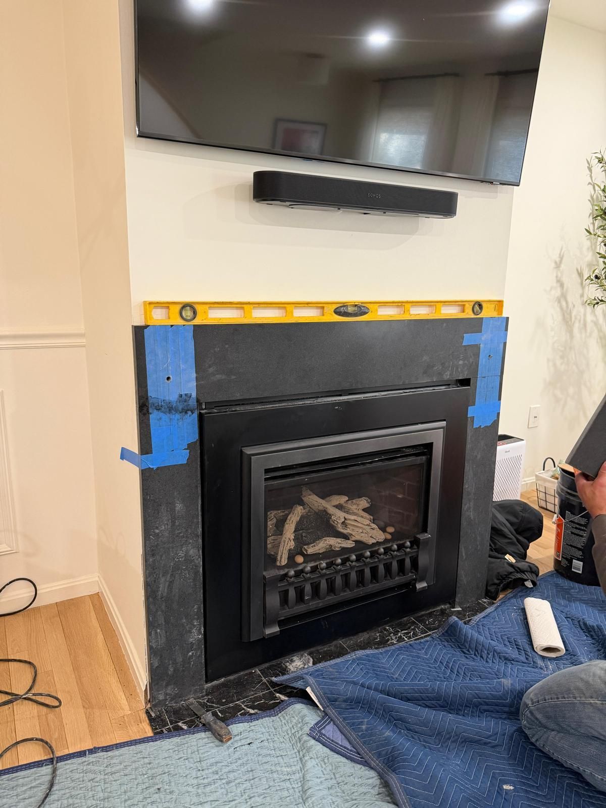 Fireplace with a black surround, level, TV, and soundbar. Blue tape secures the surround.