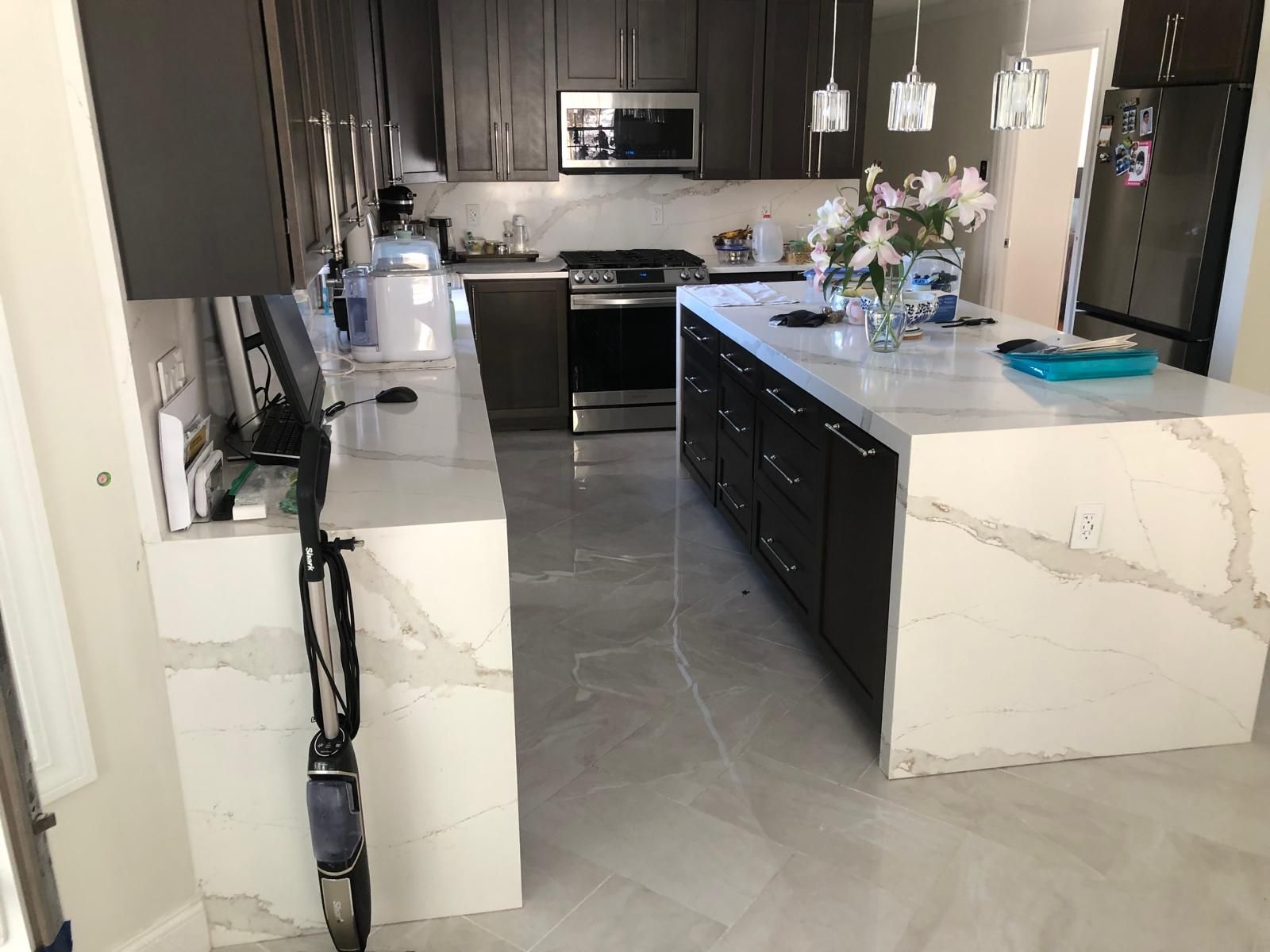 Modern kitchen with dark cabinets, white countertops, and a large island.