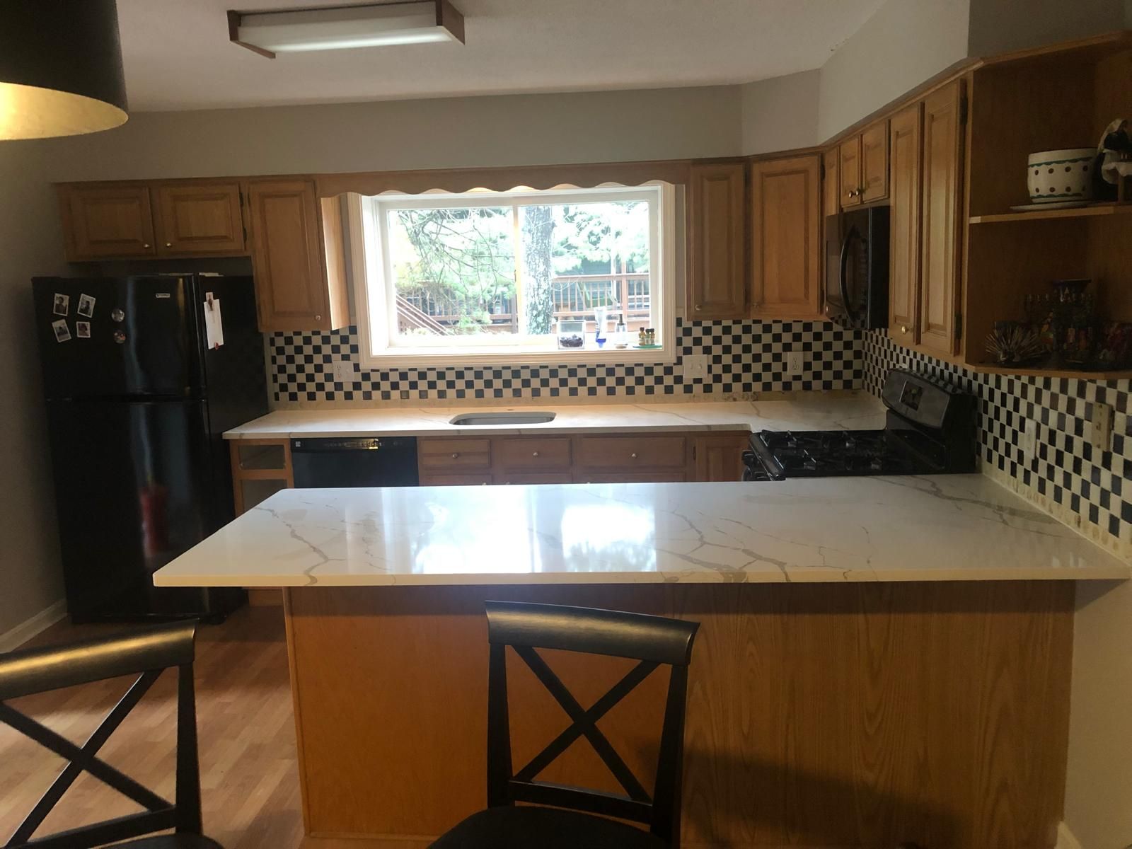 Kitchen with light wood cabinets, black appliances, white countertops, and black and white checkered backsplash.