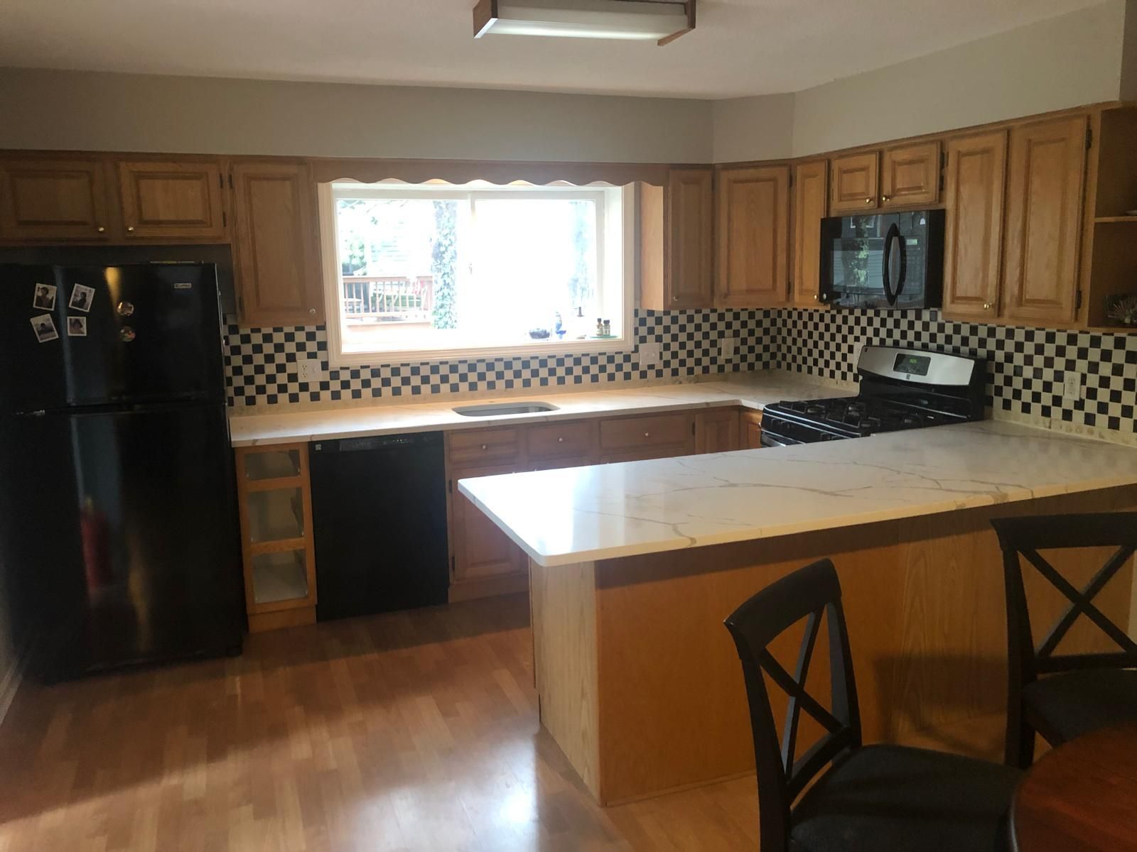 Kitchen with wood cabinets, black appliances, black and white tiled backsplash, and an island.