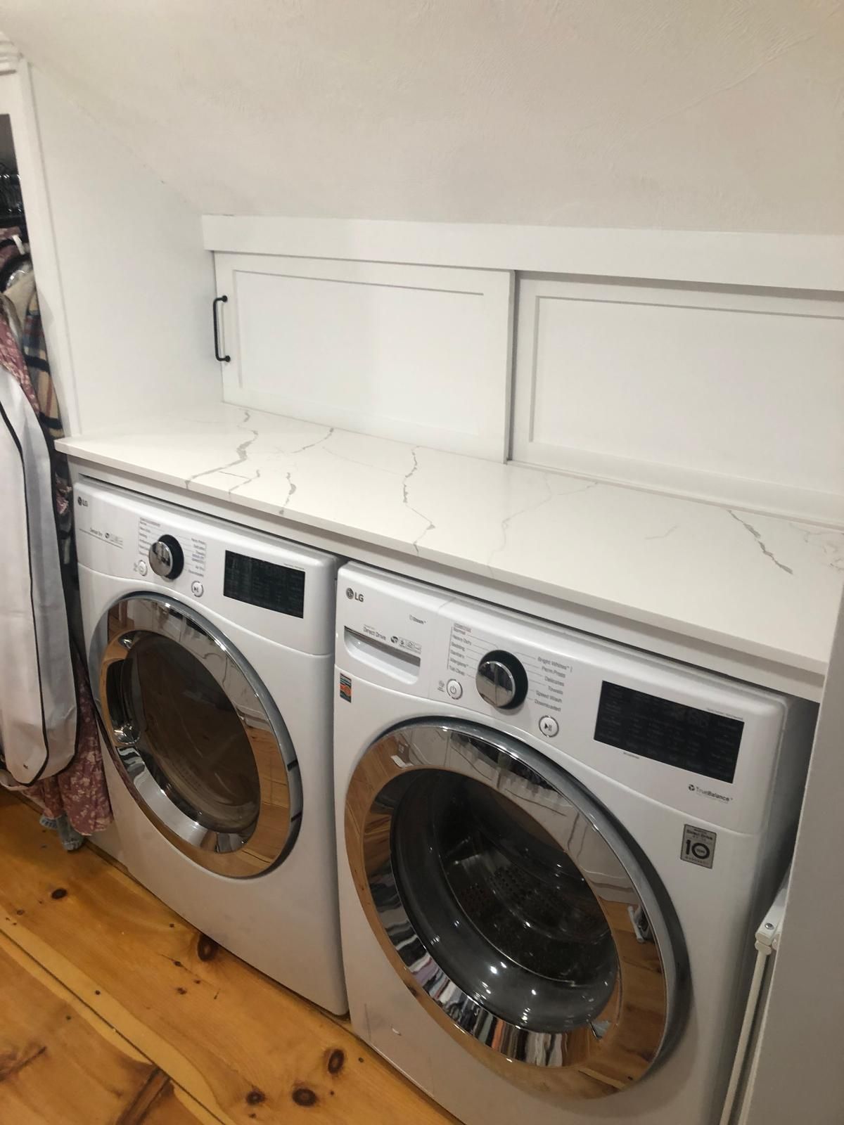 White LG washer and dryer pair with countertop, wooden floor, and storage cabinet above.