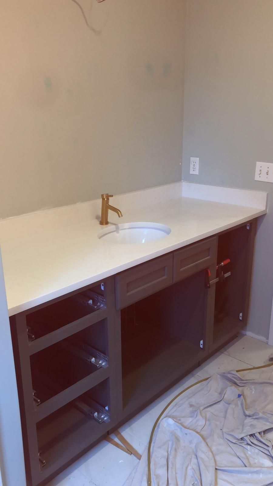 Bathroom vanity with a white countertop and gold faucet, dark brown cabinets.