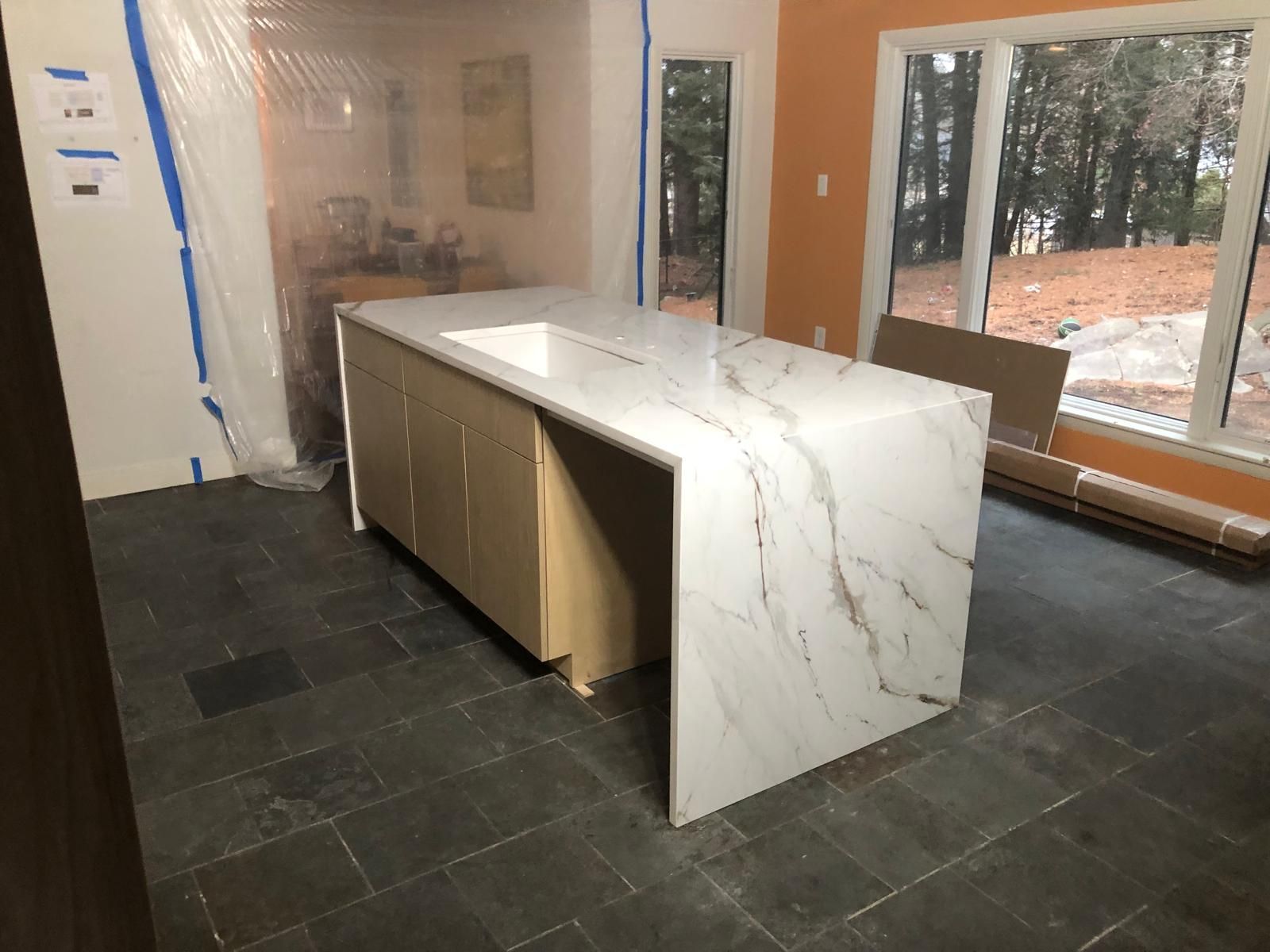 Kitchen island with marble countertop and light wood cabinets, set on dark tile floor.