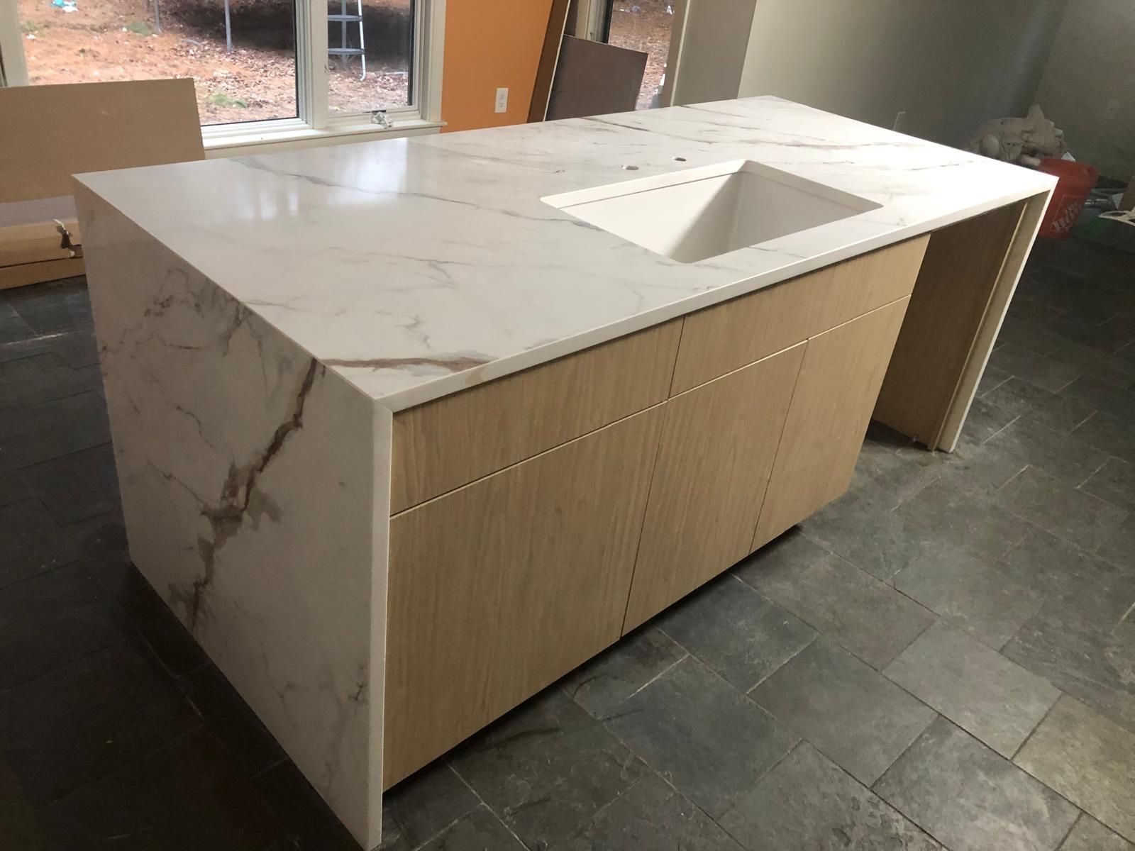 Kitchen island with light wood cabinets, white marble countertop, and built-in sink.