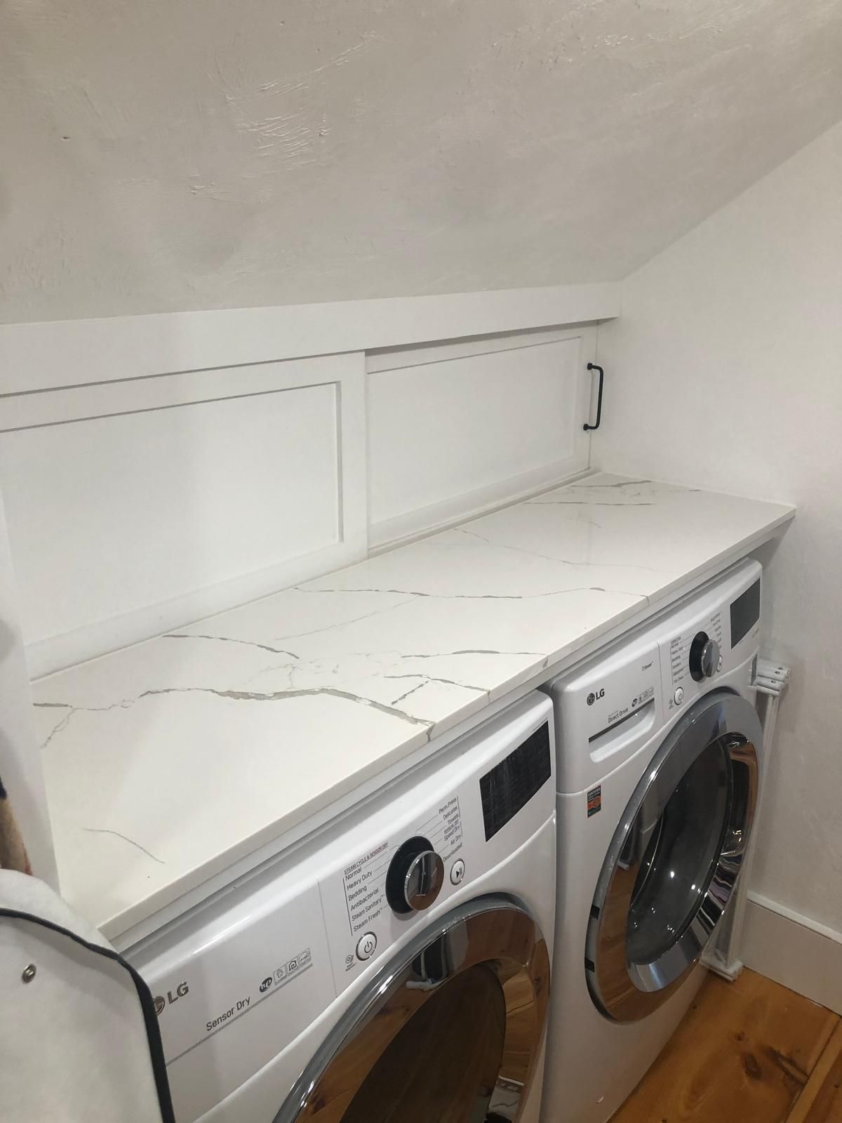 White marble countertop over a stacked washer and dryer in a laundry room.