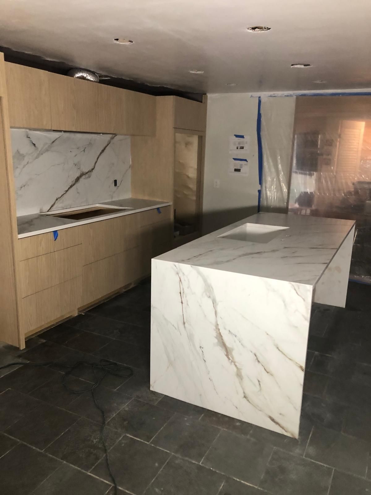 Modern kitchen under construction, featuring marble countertops and light wood cabinetry.