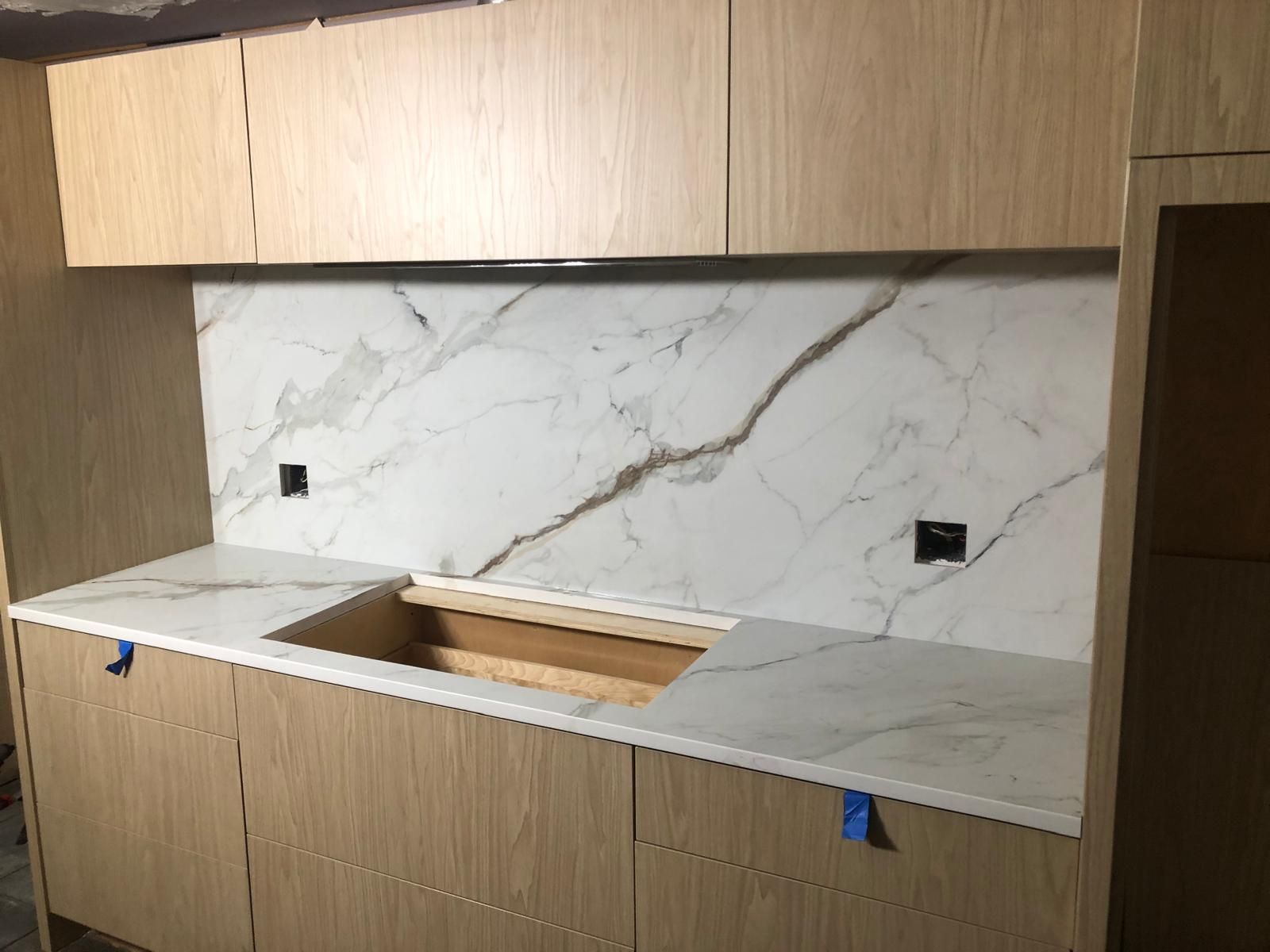 Kitchen under construction with light wood cabinets, white marble countertop and backsplash.