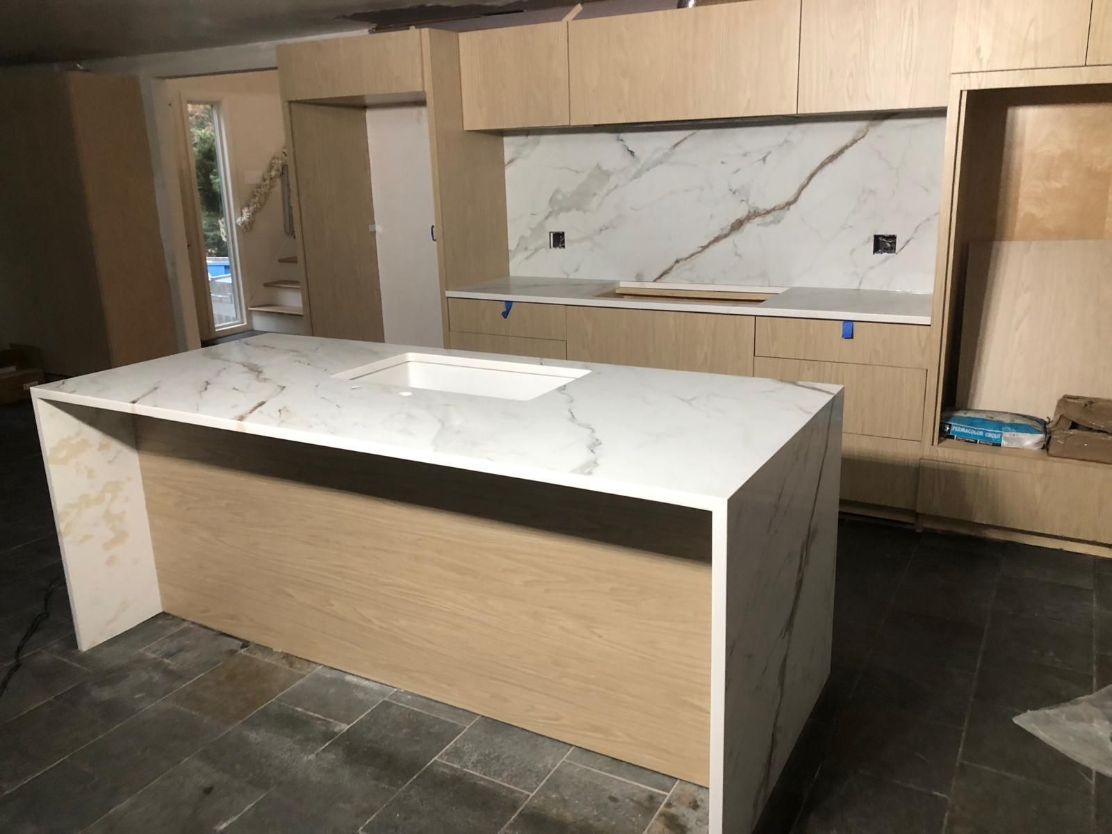 Modern kitchen under construction with a marble countertop island and light wood cabinetry.