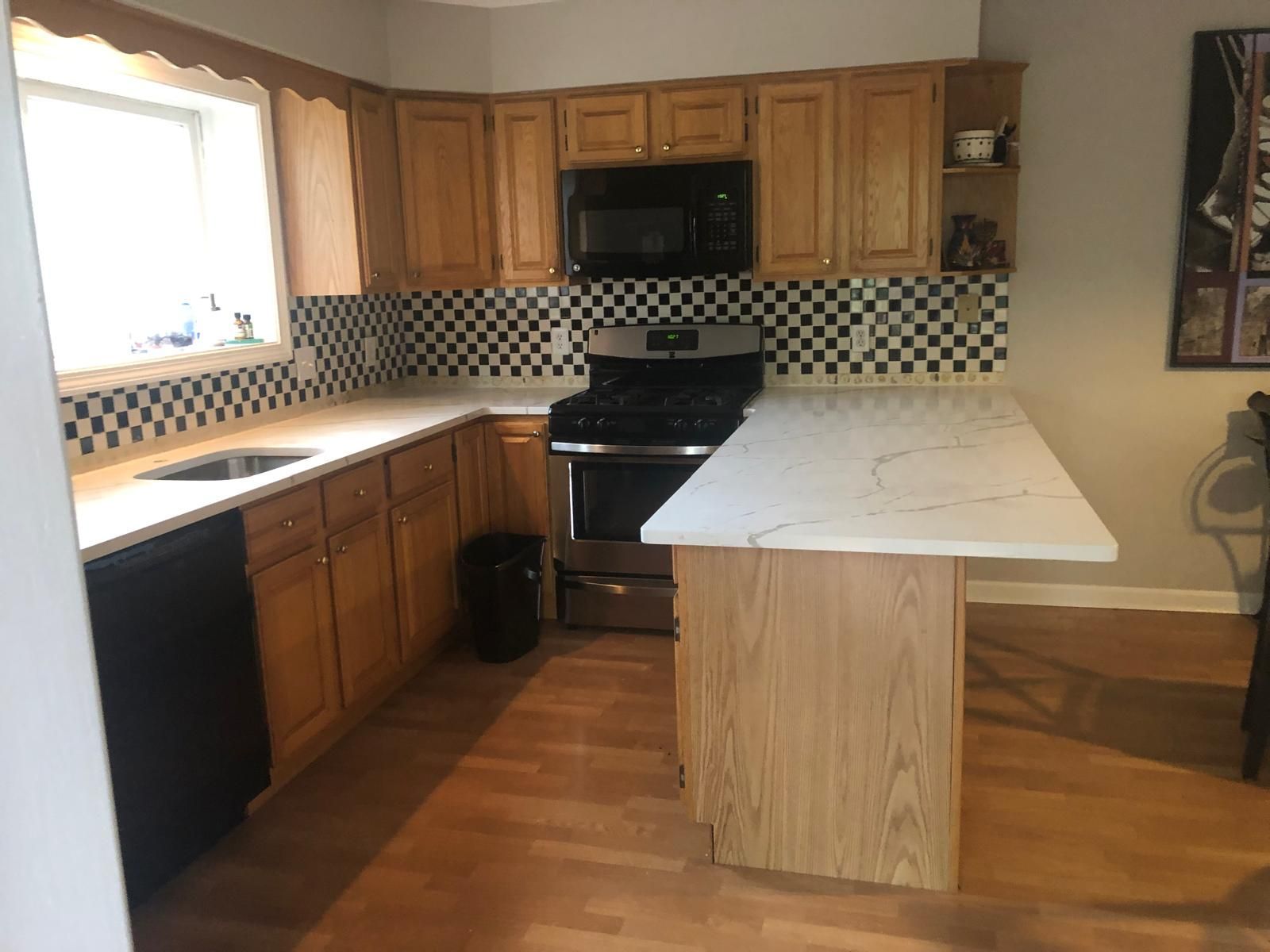 Kitchen with wooden cabinets, black appliances, checkered backsplash, and white countertops.