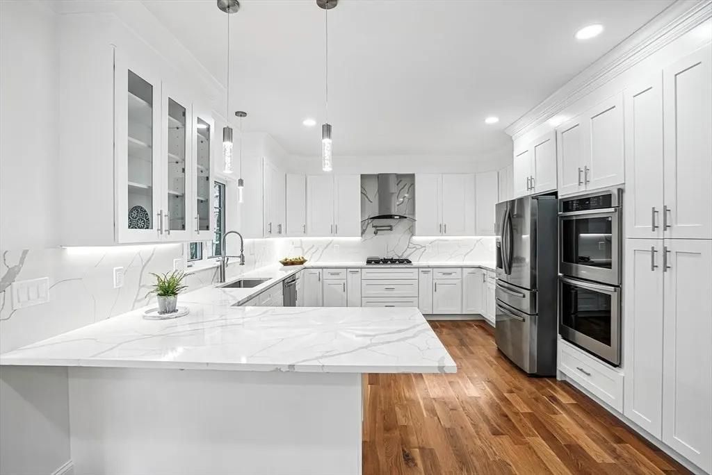 Modern white kitchen with marble countertops and stainless steel appliances; hardwood floors.