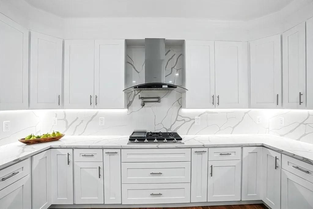 White kitchen with marble backsplash, range, and stainless steel hood.