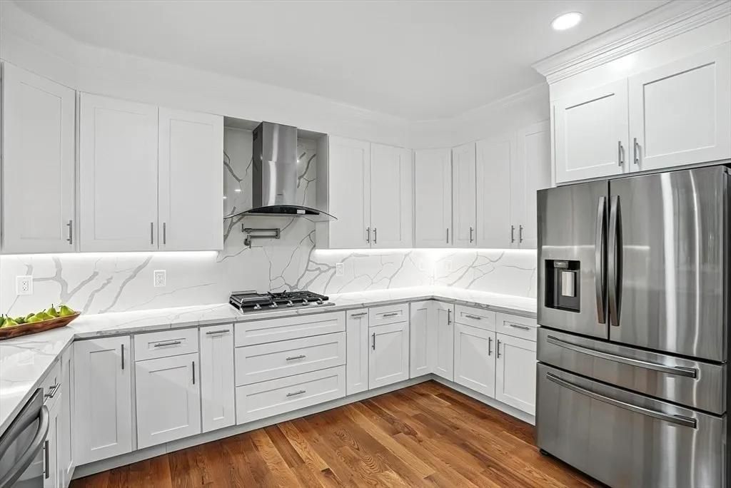 White kitchen with stainless steel appliances, wooden floors, and marble countertops.