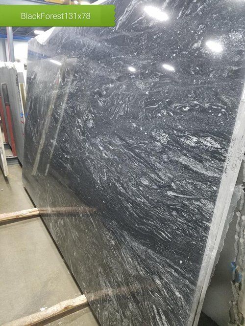 A large black granite slab is sitting on top of a wooden pallet in a warehouse.