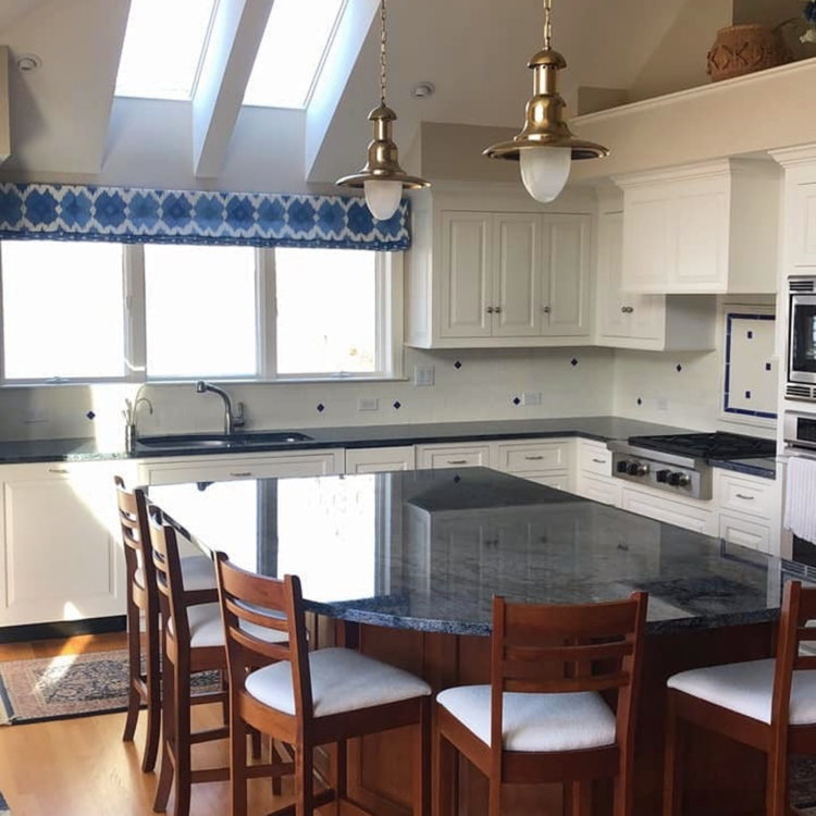 White kitchen with marble countertops, wooden floors, and stainless steel appliances.