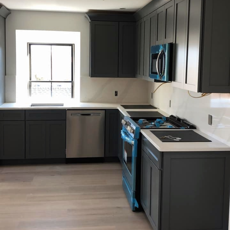 Dark gray kitchen cabinets with white countertops and a stainless steel dishwasher and oven.