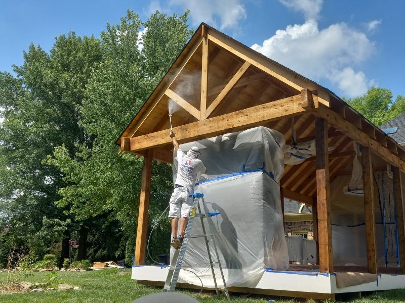 A man is spraying paint on a wooden structure.