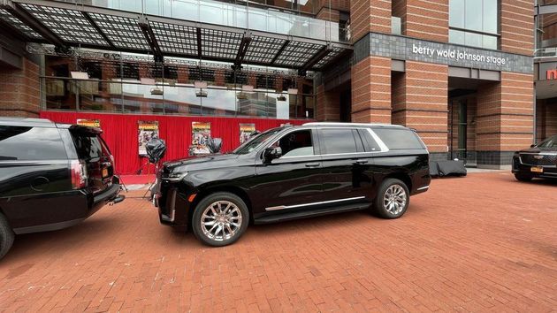 Black SUV parked on a brick plaza outside a building with red banners and a covered entrance