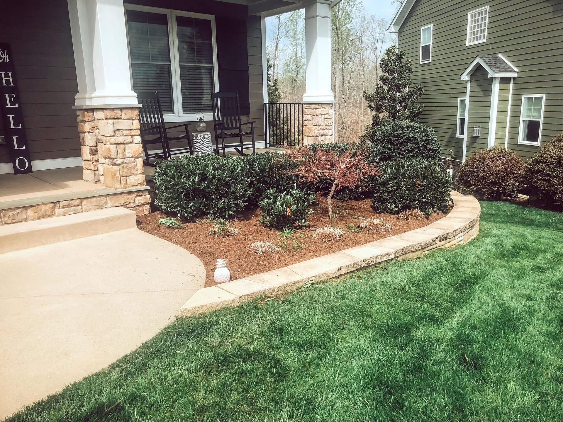 Front yard landscaping with a stone-edged flower bed in front of a house. Green grass and shrubs.