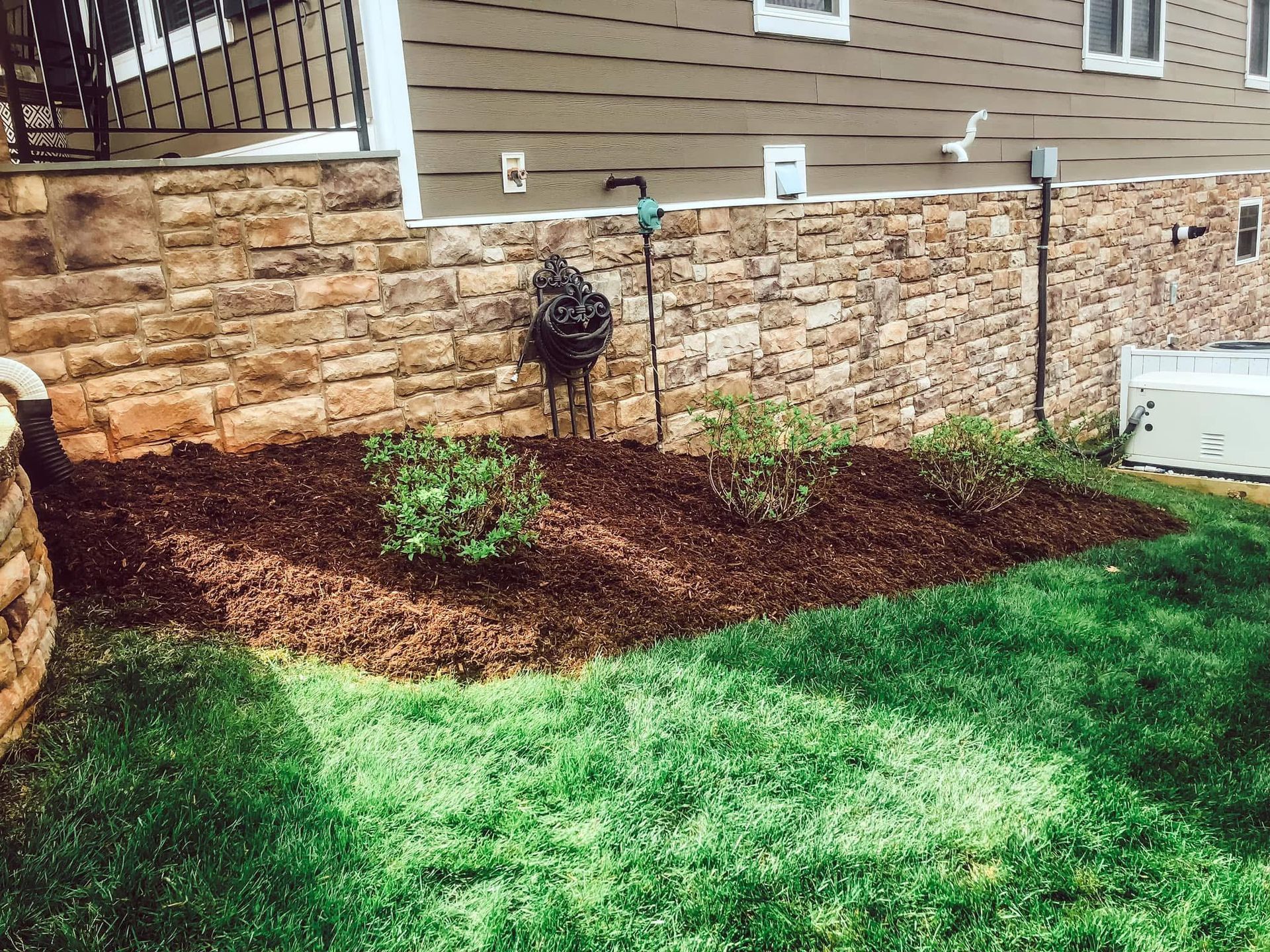Stone retaining wall with a landscaped bed of mulch and shrubbery, next to green grass.