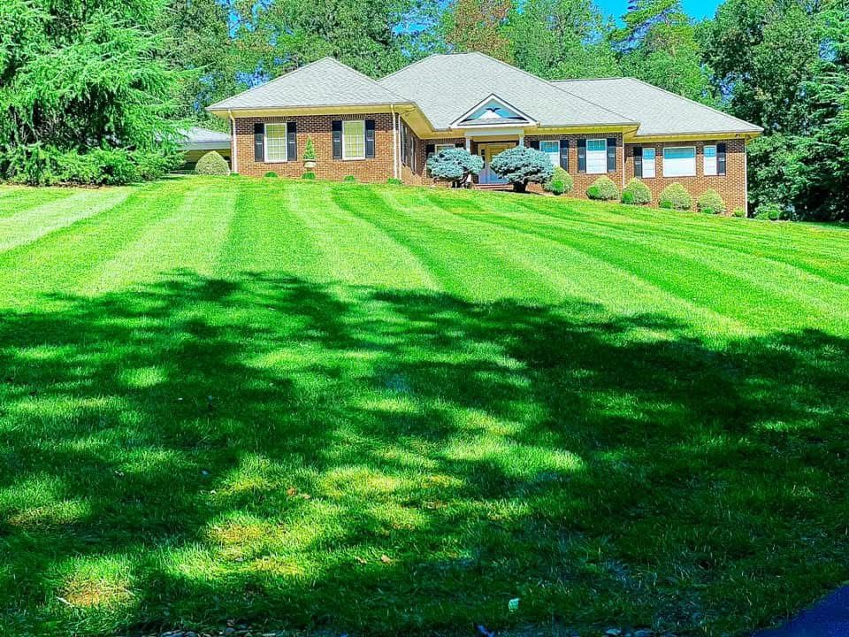 Brick house with striped green lawn under the shade of trees on a sunny day.