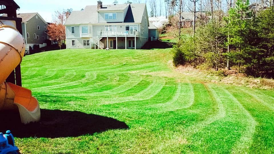 Lawn with striped mowing patterns leading up to a large two-story house.
