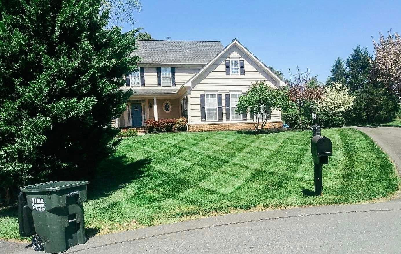Two-story house with green lawn, cut in diamond pattern; black mailbox and green trash bin on the right.