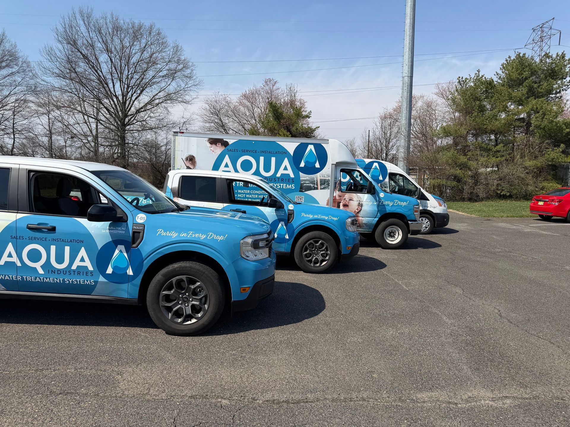 Several blue and white Aqua company work trucks parked in a gravel lot on a sunny day.