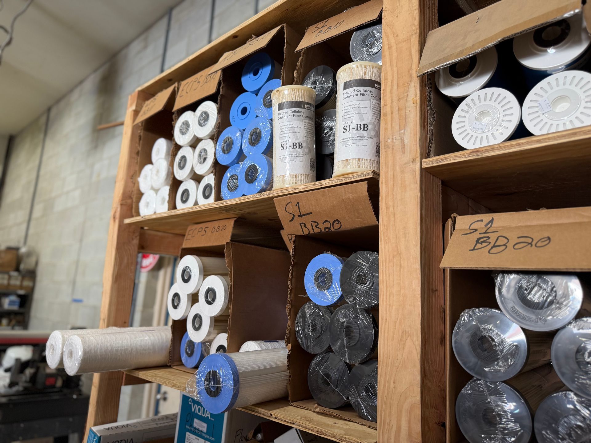 A wooden shelving unit stocked with various rolls of white and blue construction materials and labels in a workshop.