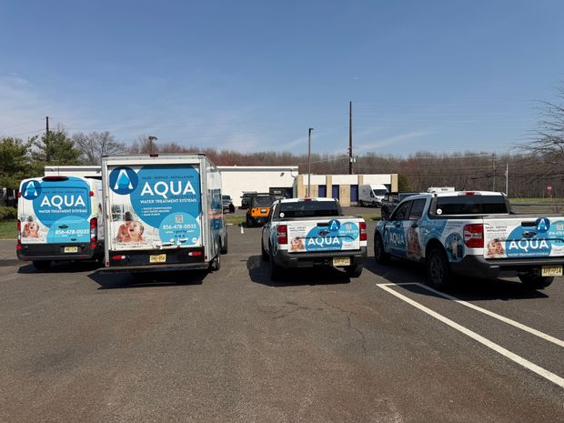 Four Aqua plumbing service vehicles parked in an outdoor lot on a sunny day.