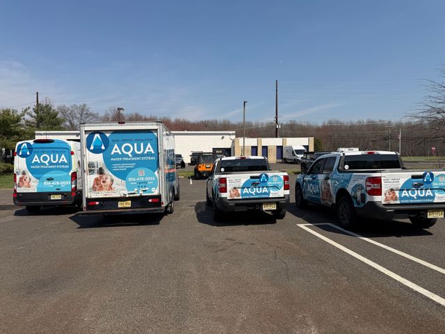 Four Aqua plumbing service vehicles parked in an outdoor lot on a sunny day.