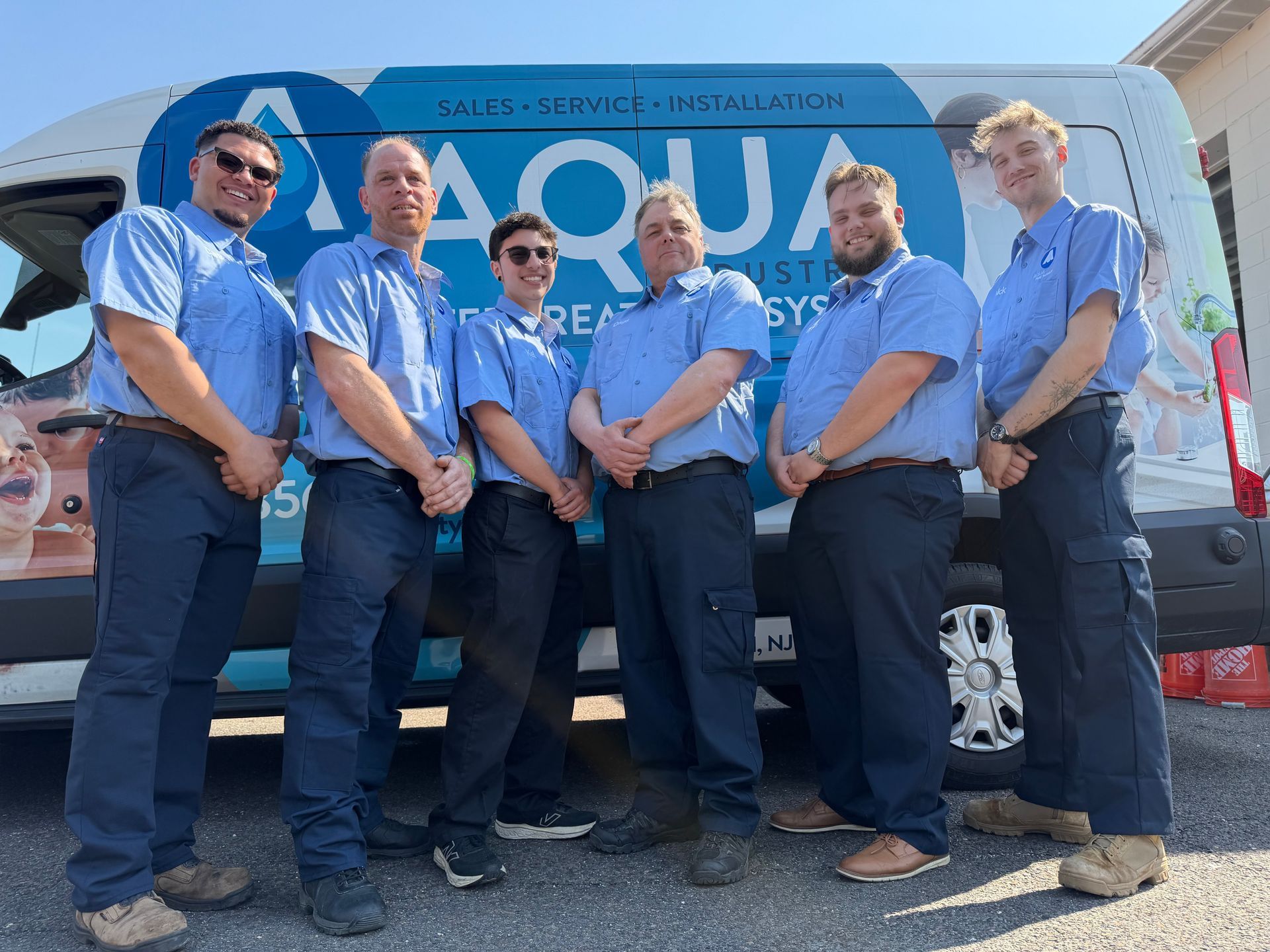Six people in blue uniforms stand in front of a white service van labeled 