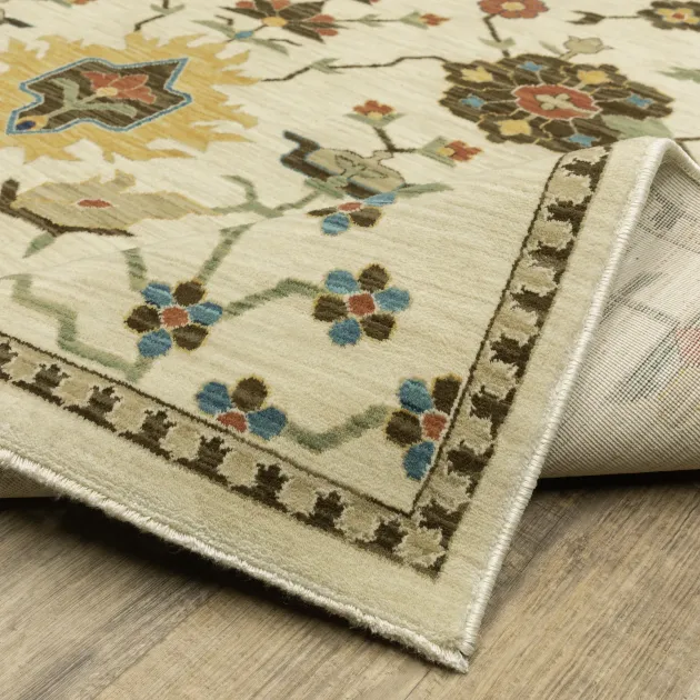 Folded cream floral rug with blue and red medallion pattern and brown border on a beige floor