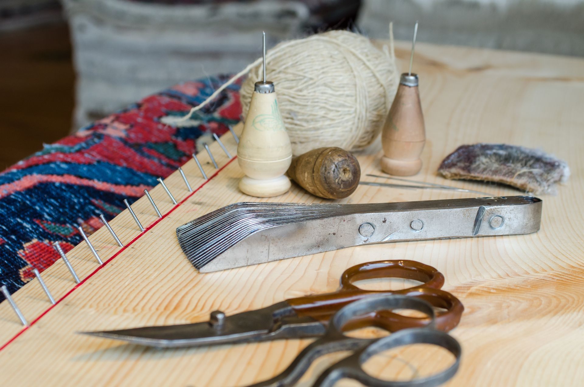 Needles, thread, scissors, and a small knife on a woven mat with yarn balls and sewing tools.