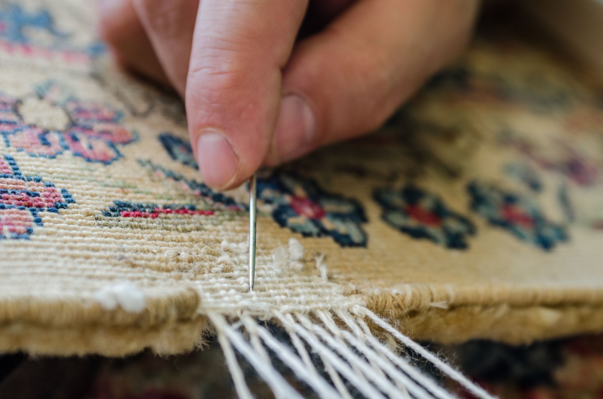 Hand weaving a patterned rug with a needle, fringe visible at the edge.