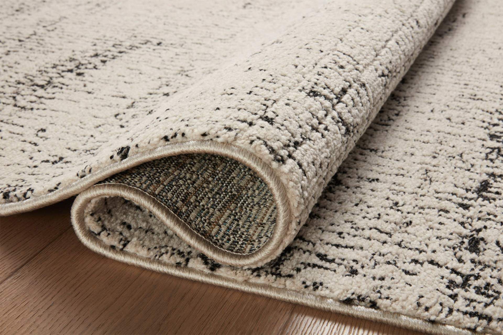 Rolled corner of a cream patterned rug on a wooden floor