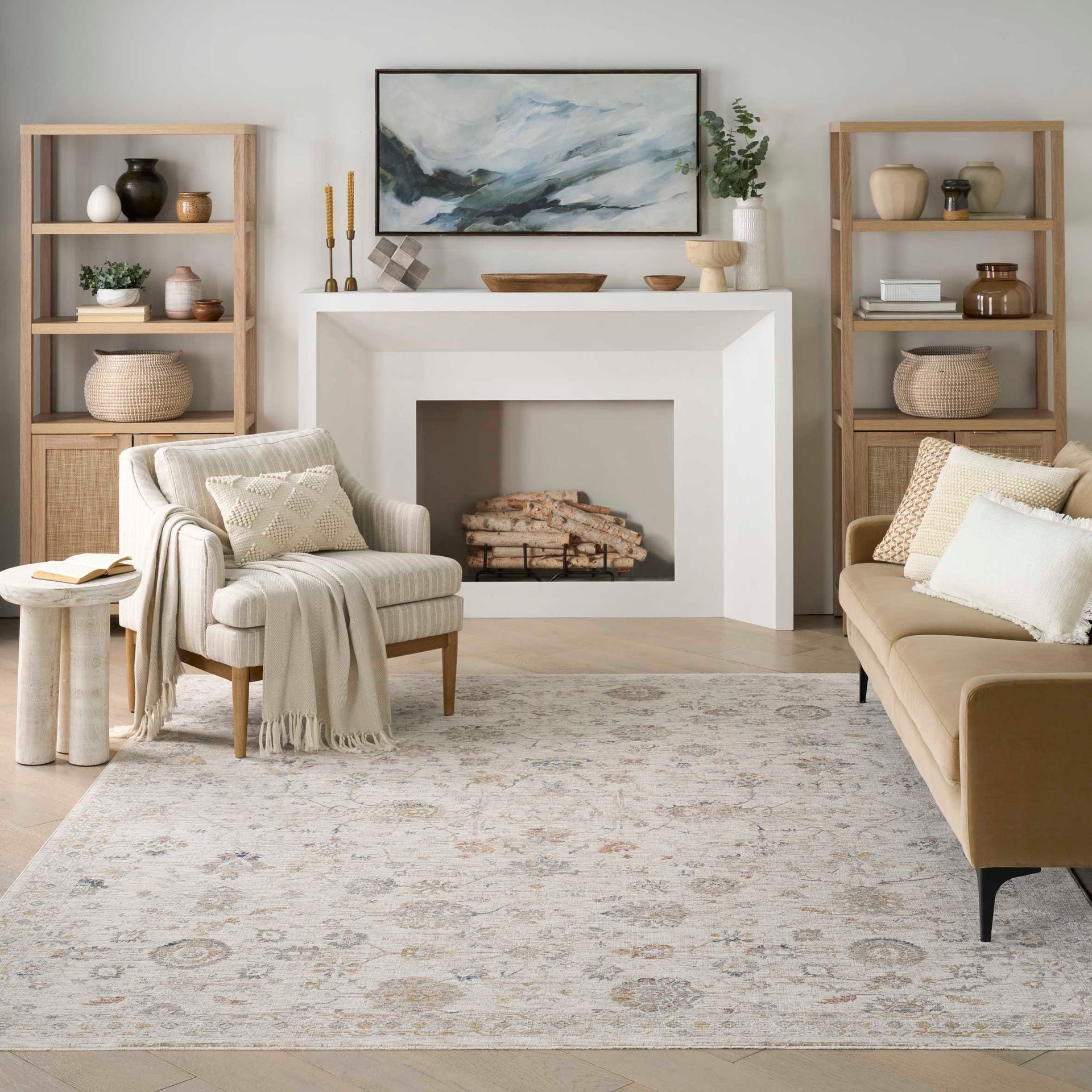 Cozy neutral living room with fireplace, beige sofa, armchair, shelving, and abstract art above the mantel