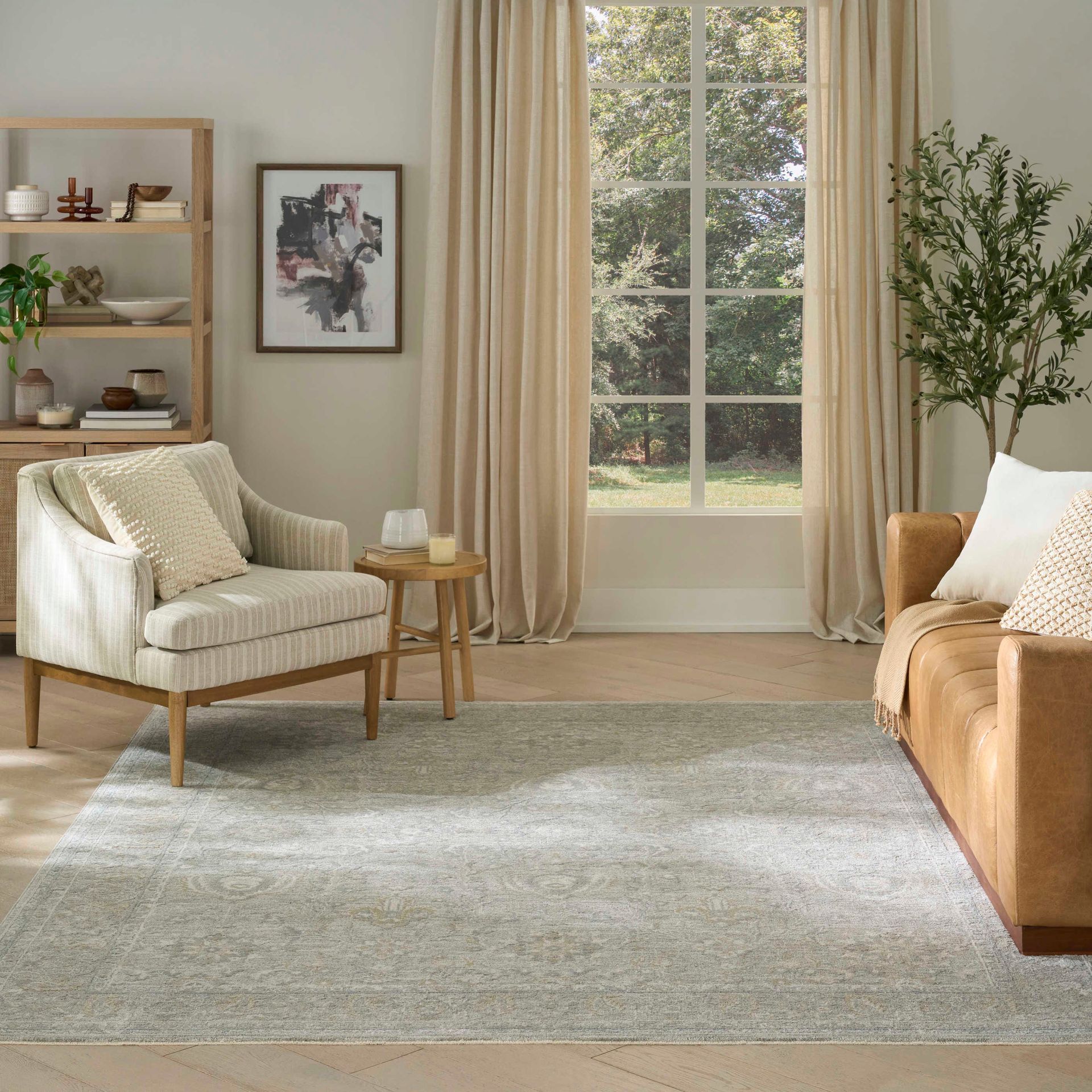 Cozy living room with cream armchair, tan sofa, green rug, tall window, and soft beige curtains