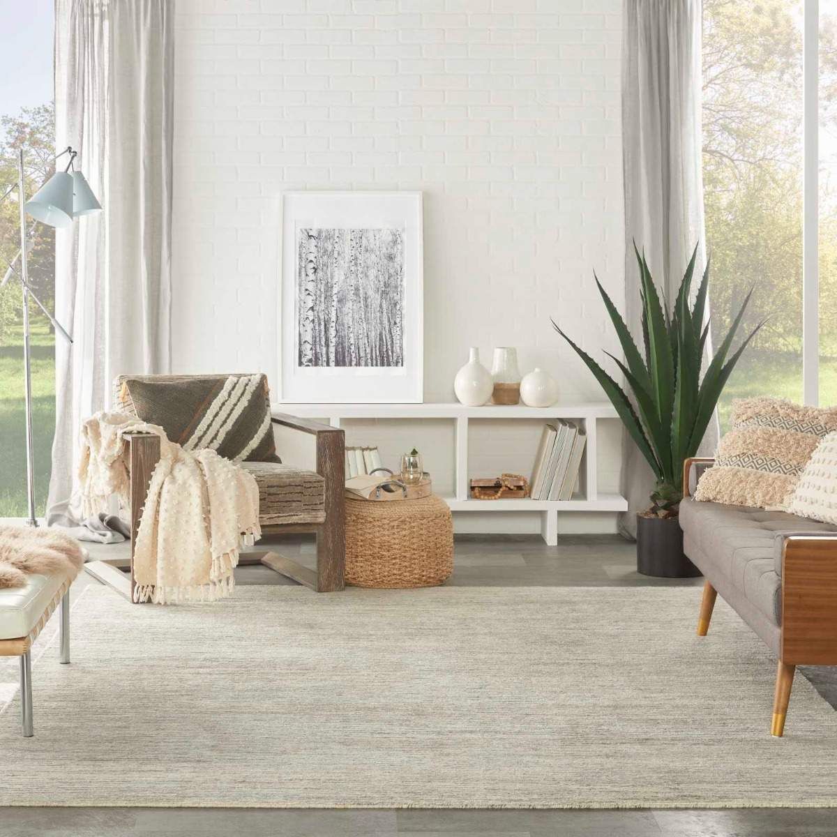 Bright airy living room with beige rug, wooden bench, woven baskets, plants, and framed art on a white wall