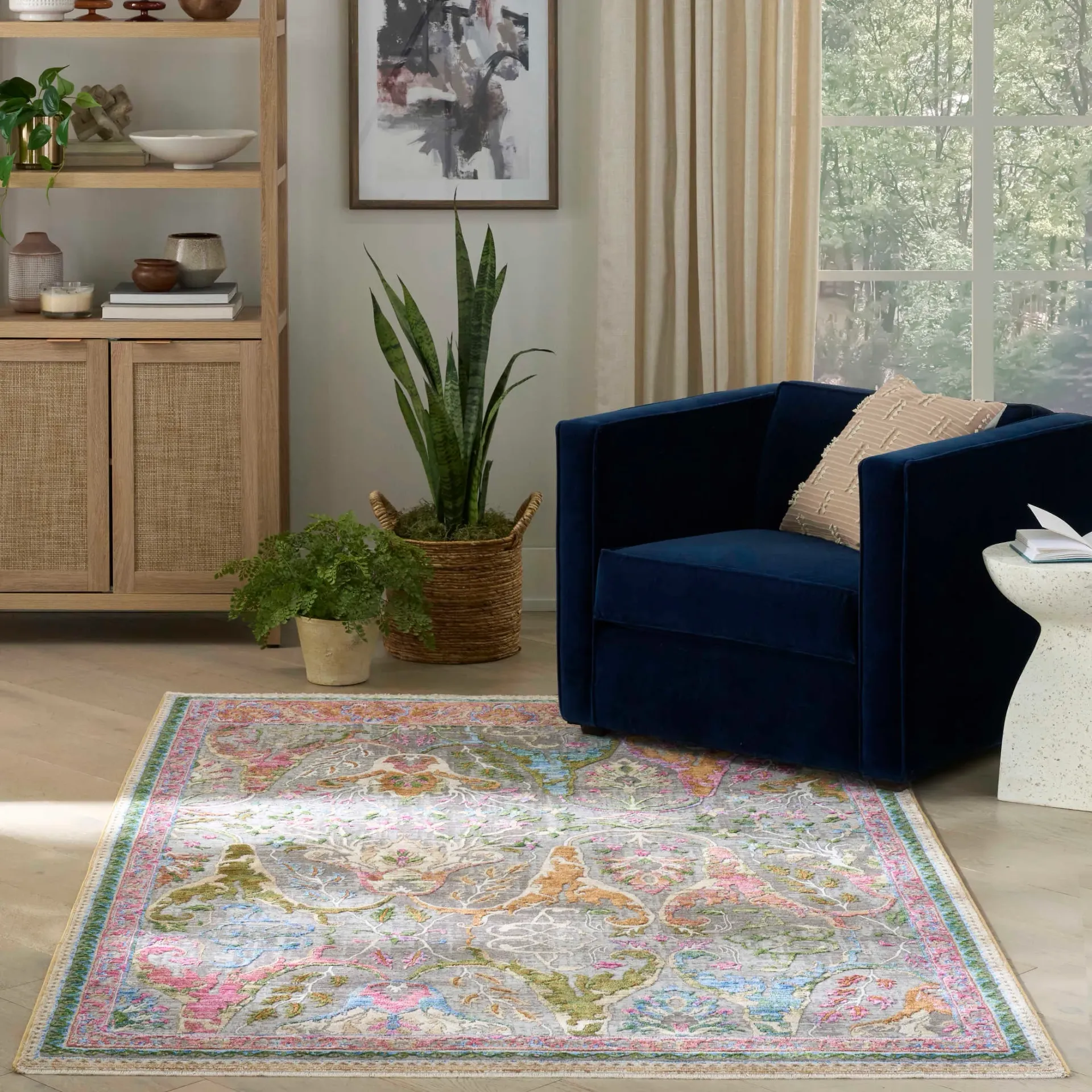 Cozy living room with navy chair, patterned rug, plant, cabinet, and sunlit window curtains