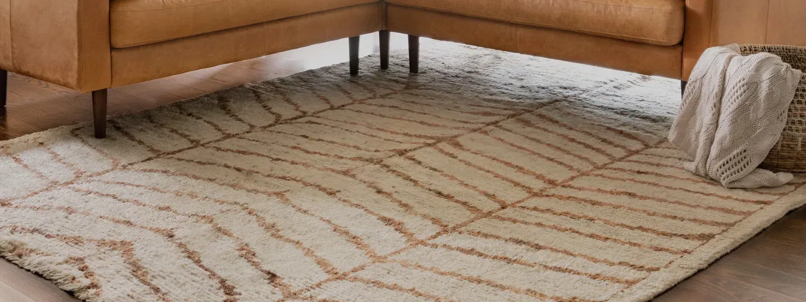 Tan rug with geometric pattern beneath a tan sofa, with a folded blanket on the right edge