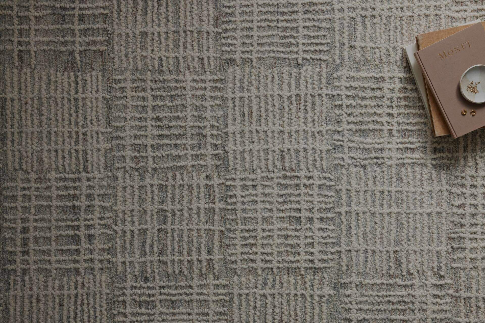 Gray woven rug with a subtle crosshatch pattern, with a notebook and cup in the top-right corner.