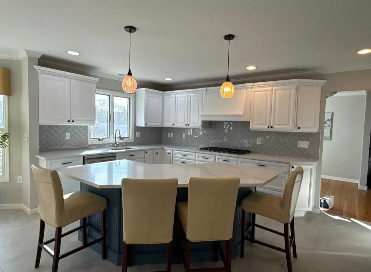 Bright kitchen with white cabinets, gray backsplash, island seating, and pendant lights.