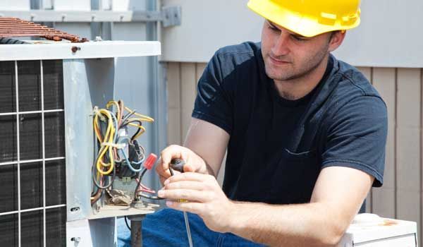 A man wearing a hard hat is working on an air conditioner.