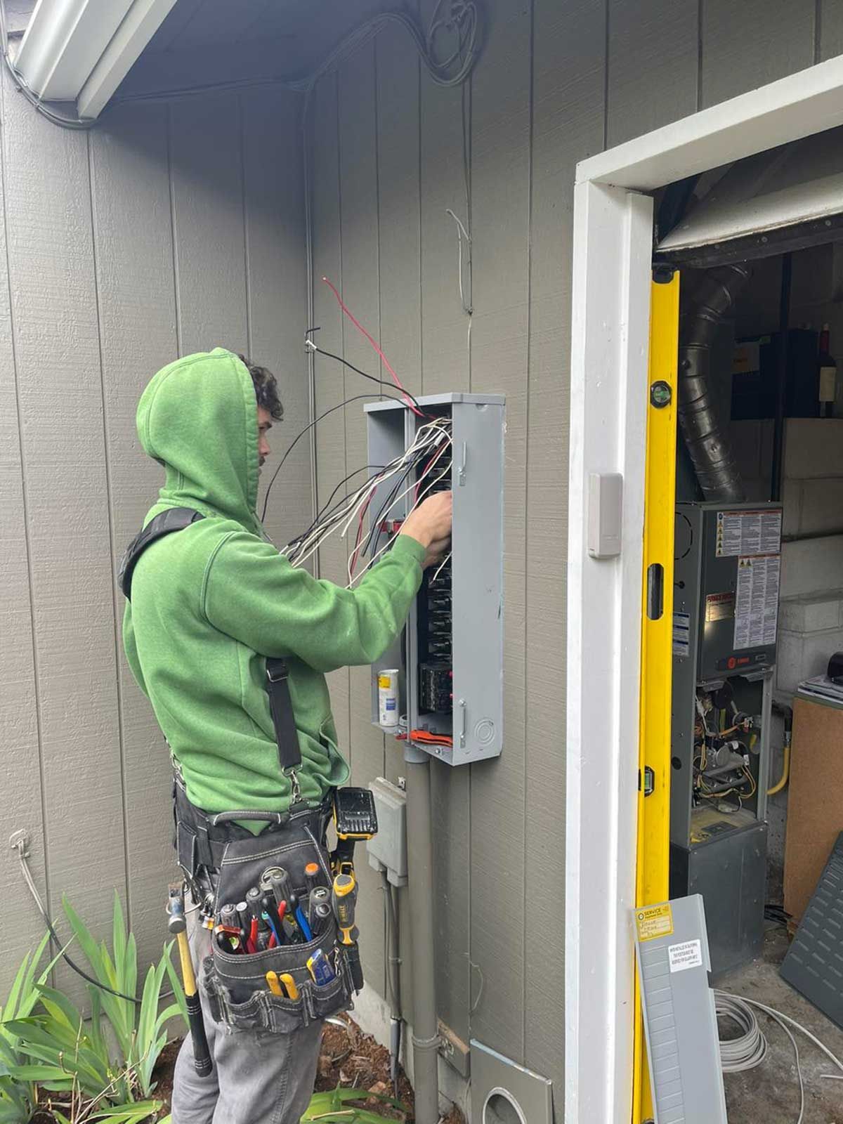 A man in a green hoodie is working on an electrical box.