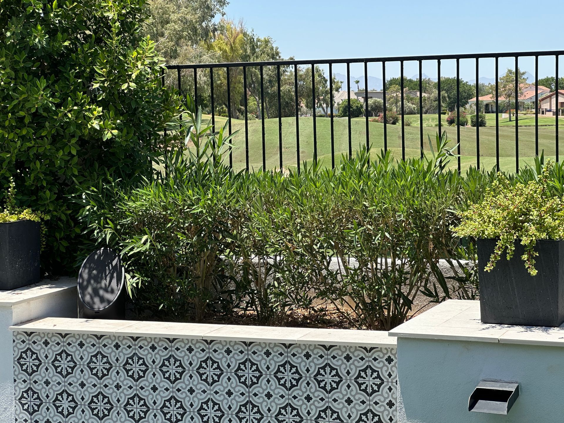 Poolside garden with patterned tile wall, greenery, black fence, and view of landscape.